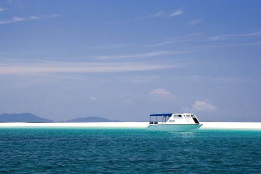 Image of a remote Malaysian tropical island with deep blue skies, crystal clear waters and a boat by the shore.