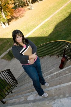 A young woman walking on campus on a nice day with her books and backpack.