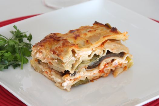 Vegetarian lasagna with eggplant, courgette, sweet potatos and tomato sauce on a white plate.