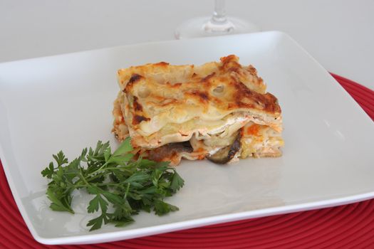 Vegetarian lasagna with eggplant, courgette, sweet potatos and tomato sauce on a white plate.