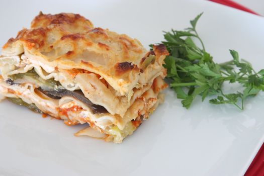 Vegetarian lasagna with eggplant, courgette, sweet potatos and tomato sauce on a white plate.