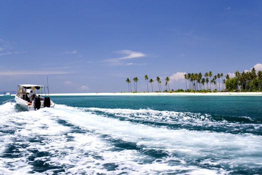 Image of boats at a remote Malaysian tropical island with deep blue skies, crystal clear waters and coconut trees.