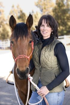 A pretty woman standing beside her pretty bay horse after an afternoon ride.