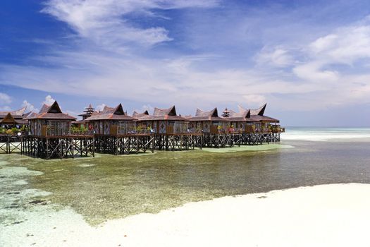 Image of huts on stilts on a remote Malaysian tropical island with deep blue skies and crystal clear waters.