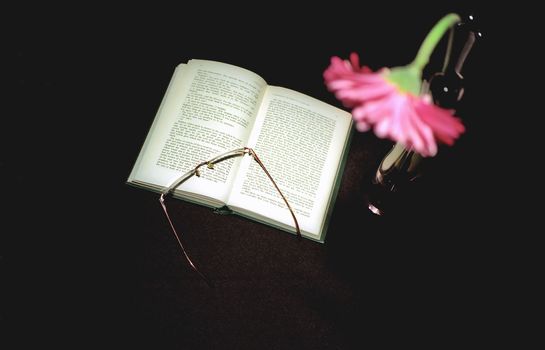 Open book and glasses on black background