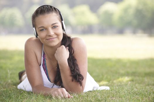 young attractive girl lying on grass wearing headphones while listening to music 