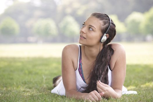 young attractive girl lying on grass wearing headphones while listening to music