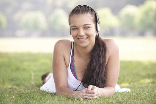 young attractive girl lying on grass wearing headphones while listening to music