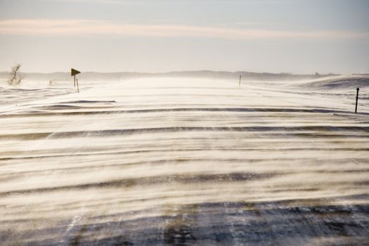 Ice covered road with snow being blown over.