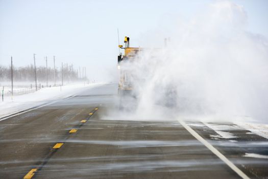 Truck on road trailing snow behind.