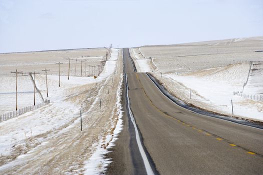 Road over rolling hill landscape with snow and power lines.