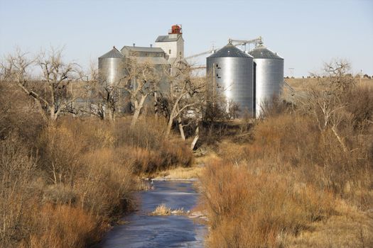 Storage silos by creek in rural setting.