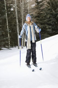 Mid adult Caucasian female skier wearing blue ski clothing standing on ski slope smiling.