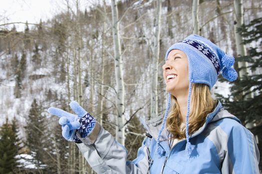 Attractive smiling mid adult Caucasian blond woman wearing blue ski clothing smiling and pointing.