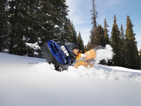 Young man digging out snowmobile submerged in the snow.