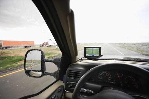 Vehicle dashboard with GPS and view through windshield of rainy highway ahead.