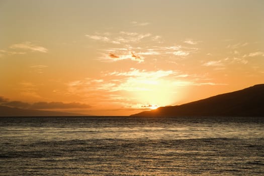 Sun setting behind island off Maui, Hawaii.