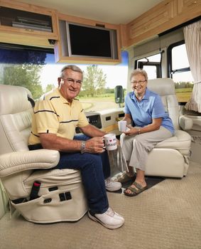 Senior couple sitting in RV holding coffee cups and smiling.