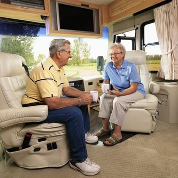 Senior couple sitting in RV holding coffee cups and smiling.