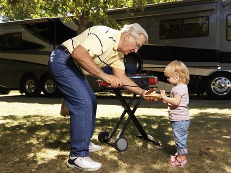 Grandfather giving granddaughter hotdog by RV.