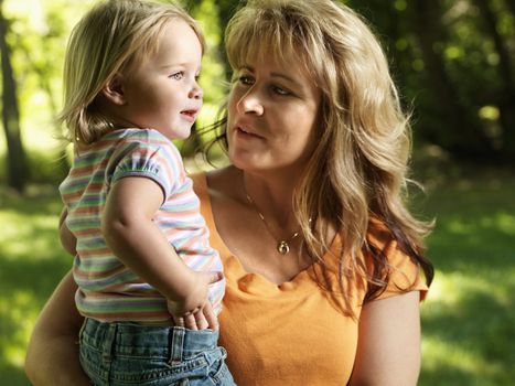 Caucasian mid adult woman holding female toddler daughter in arms at park.