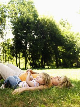 Caucasian mid adult woman with toddler daughter lying in grass at park relaxing.