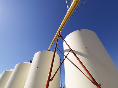 Low angle view of metal grain storage silos against blue background.