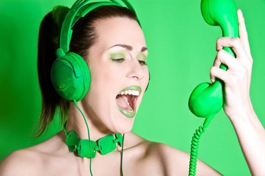 Beautiful brunette with green headphones screaming into a green phone