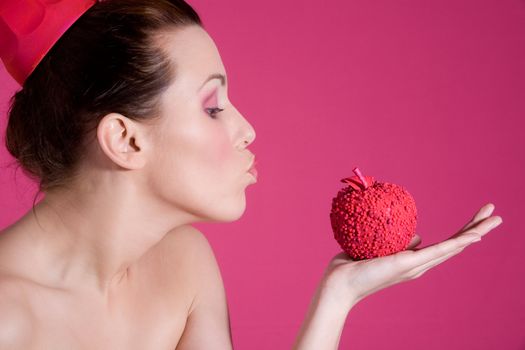 Pretty girl on pink background blowing a kiss to a pink apple