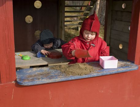 Children playing shop, one making sand cakes in the front, the other stealing the toys behind her. 