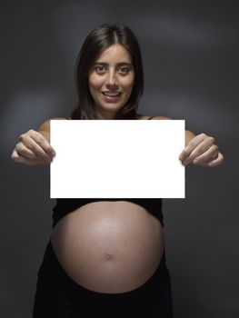 Pregnant woman holding a white card over a gray background.