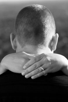 A young happy couple that is newly engaged with the woman placing her hands around her fionces neck.  Shallow depth of field with focus on the diamond engagement ring.