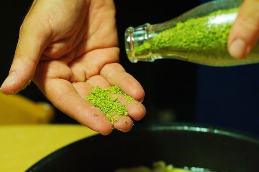 Close up pouring coriander from a bottle to an open hand while cooking focaccia