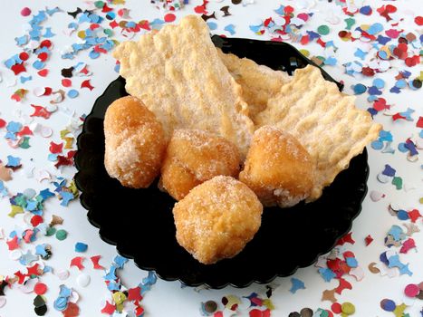 Carnival cakes in black dish on background of confetti