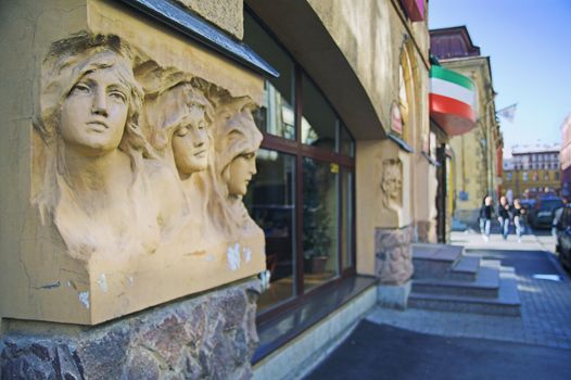 Entrance to cafe in city street with a group of people in background. The building was built before 1900, and the sculptures on the facade are public monuments and nobody can have copyright on them.