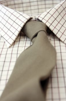 A close up view of a mans cotton checked shirt with a matching gray colored woolen tie. Low angled view with focus to middle.