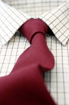 A close up view of a mans cotton checked shirt with a matching burgundy colored woolen tie. Low angled view with focus to middle.