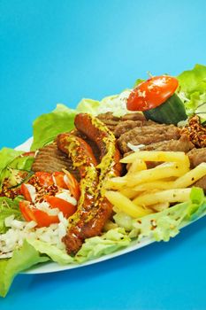 Arranged grill meat with sausages and fried potato on the oval plate decorated with salad and vegetables