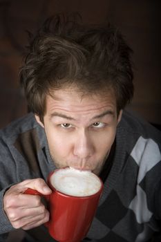 Young man drinking speialty coffee drink from red mug