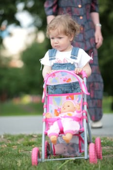 little girl walks in park with doll in sidercar