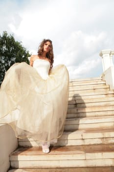 vertical portrait of the bride in white-golden gown on background blue sky with clouds