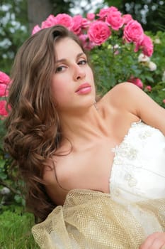 portrait of the beautiful girl in white-golden gown on background of the rosebush