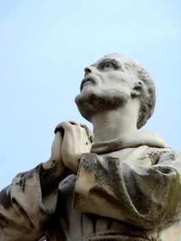 White statue of a praying monk viewed from under