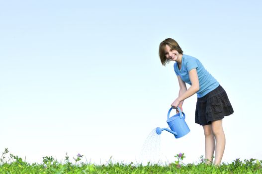 Smiling teenage girl with watering can on green grass