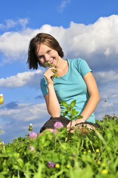 Young teenage girl sitting on grass and smelling a flower