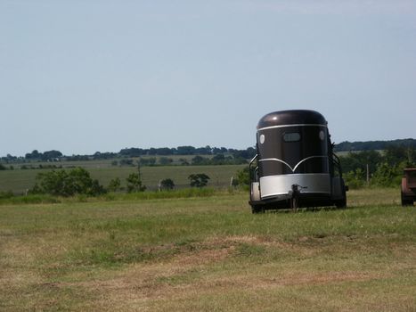 A horse trailer parked in a pasture out in the country.