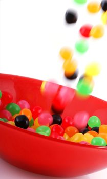 Colorful jelly beans falling into a red bowl. 