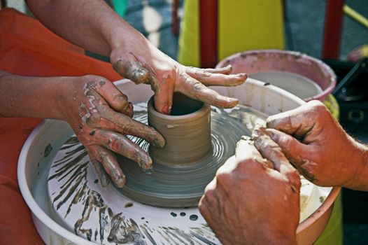 potter's hands guiding woman's hands to help her learn pottery