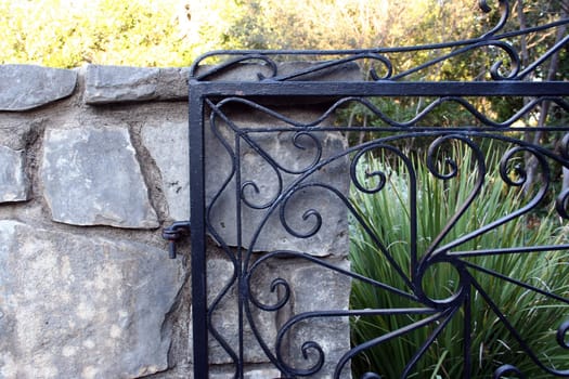 An artistic shot of an old steel gate connected to a stone wall.