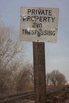 no trespasing, private property sign at a railroad with holes from shotgun and bullets